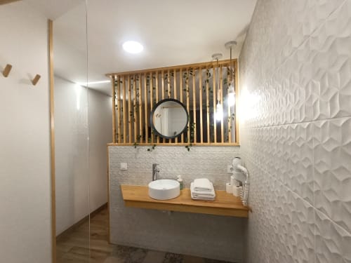 Baño moderno en apartamento El Rincón de Sevilla con azulejos blancos texturados, vanidor de madera, espejo redondo y lavamanos de recipiente