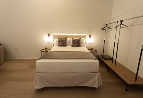 Dormitorio moderno en apartamento El Rincón de Sevilla con cama de matrimonio, apliques de pared, mesitas de noche de madera y prendas de vestir