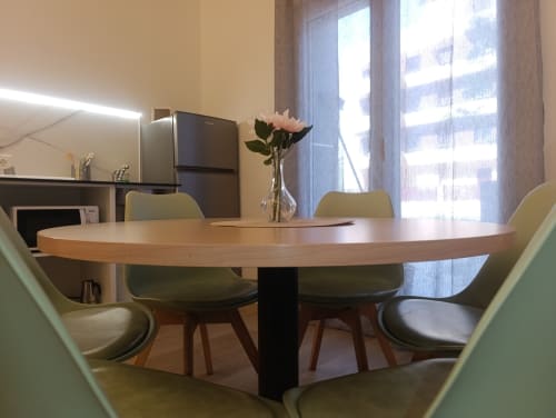Comedor moderno en apartamento El Rincón de Sevilla con mesa redonda de madera, sillas verdes, cocineta y ventanas luminosas
