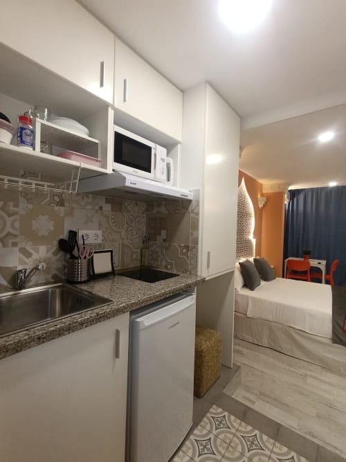 Moderna cocina equipada con muebles blancos, microondas y encimera de granito en apartamento Al-Ándalus, Sevilla