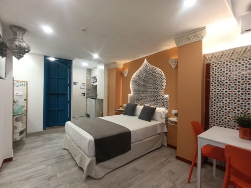 Habitación de apartamento Al-Andalus en Sevilla con cabecero estilo marroquí, paredes naranjas y comodidades modernas cerca del metro