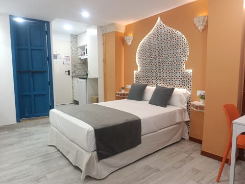 Habitación moderna en El Rincón de Sevilla con cabecero morisco ornamentado, paredes naranjas y puerta azul de entrada en apartamento sevillano.