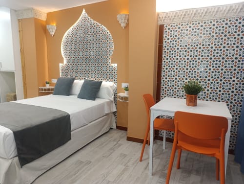 Dormitorio moderno en El Rincón de Sevilla con cabecero estilo marroquí, cama blanca, sillas naranjas y azulejos geométricos