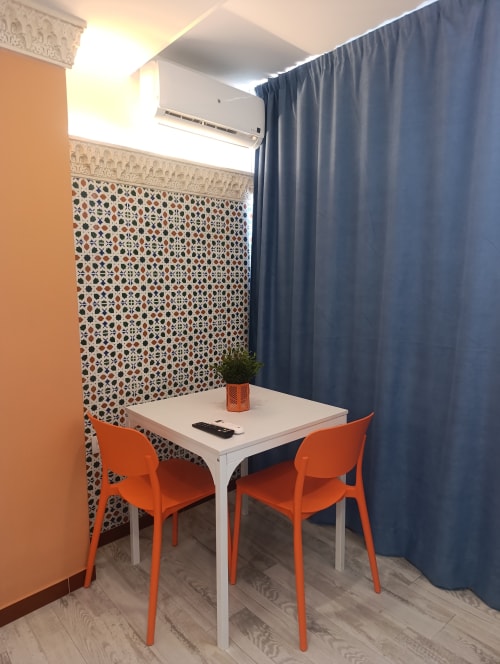 Moderno rincón de estudio en El Rincón de Sevilla con escritorio blanco, sillas naranjas, pared de azulejos decorativos y cortinas azules en Sevilla