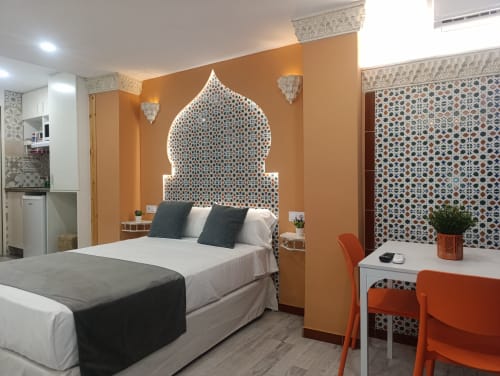 Dormitorio del apartamento Al-Andalus en Sevilla con pared acentuada en naranja, cabecero estilo marroquí ornamentado y mobiliario moderno
