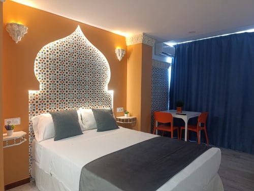 Dormitorio moderno en hotel El Rincón de Sevilla con cabecero de estilo islámico ornamentado, cama blanca, paredes naranjas y detalles azules