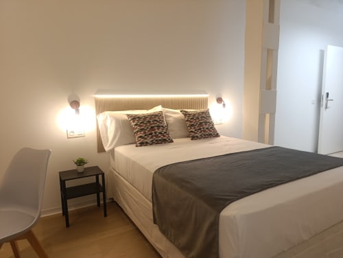 Dormitorio moderno en El Rincón de Sevilla con cama matrimonial, iluminación ambiental, cabecero de madera y almohadas estampadas