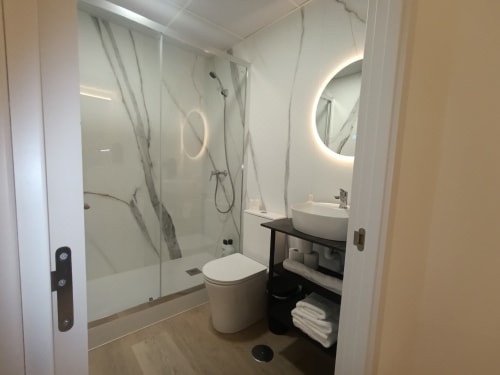 Baño moderno en el apartamento El Rincón de Sevilla con ducha, inodoro, espejo redondo y lavamanos