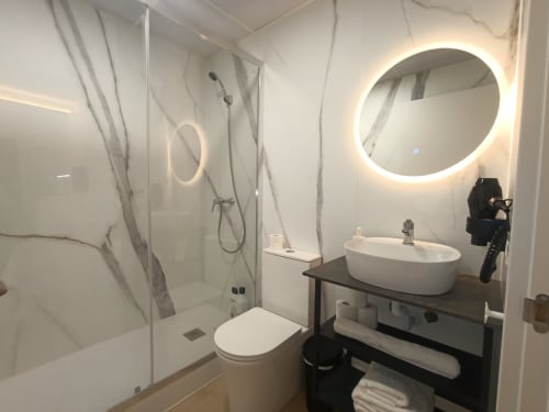Baño moderno en apartamento El Rincón de Sevilla con espejo iluminado, lavamanos blanco, inodoro y ducha con mampara de cristal