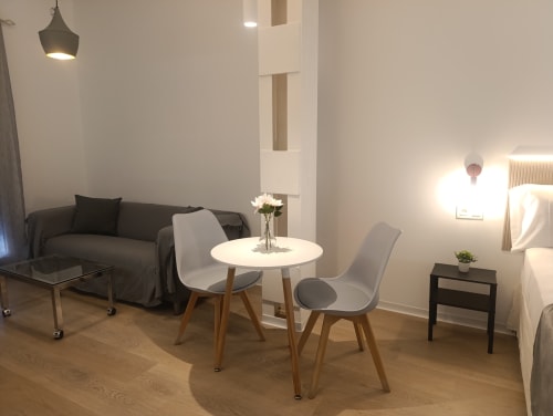 Moderno estudio en El Rincón de Sevilla con sala de estar, mesa redonda blanca, sofá oscuro y suelos de madera