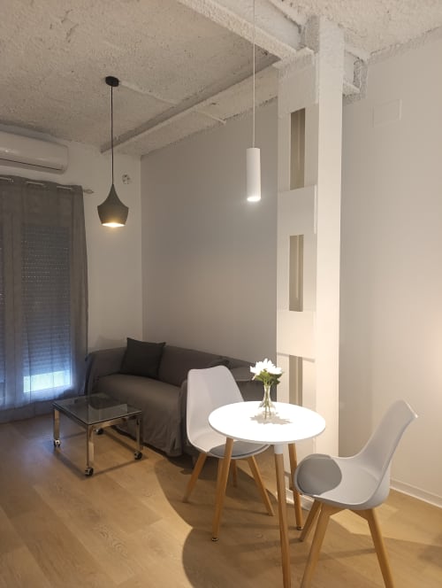 Sala moderna en apartamento El Rincón de Sevilla con sofá, mesa redonda blanca, sillas de madera, iluminación colgante y