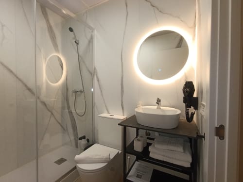 Baño moderno en El Rincón de Sevilla con azulejos de mármol, espejos LED redondos, lavabo blanco y ducha a ras de suelo