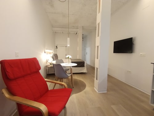Sala de estar moderna en El Rincón de Sevilla con sillón rojo, sofá, televisor y distribución abierta en apartamento sevillano