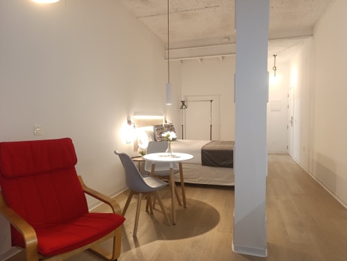 Estudio moderno en El Rincón de Sevilla con silla roja, cama, mesa redonda blanca y decoración minimalista