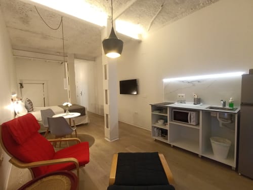 Moderno apartaestudio en Sevilla con sillón rojo, cocina americana, zona de descanso y TV de pantalla plana