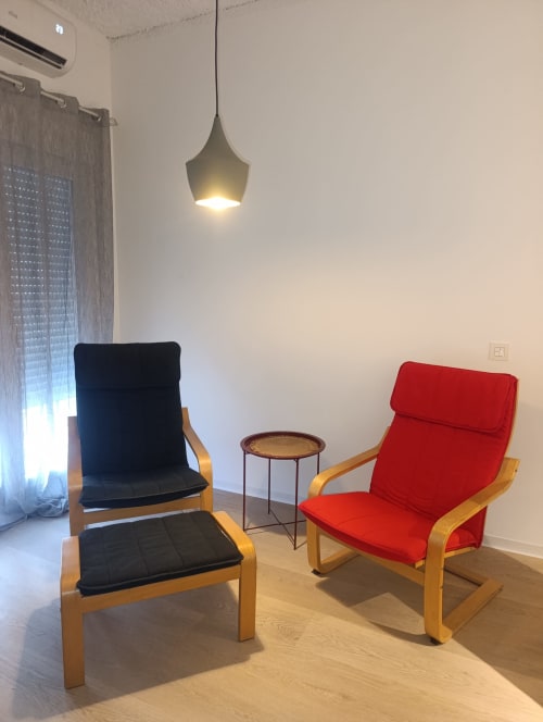 Sala de estar moderna en El Rincón de Sevilla con sillones negros y rojos, marcos de madera, mesa auxiliar e iluminación colgante
