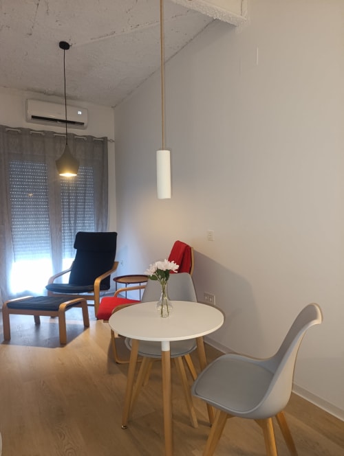 Sala de estar moderna de apartamento con mesa redonda blanca, sillas de madera, iluminación colgante y cómodos asientos en El Rincón de