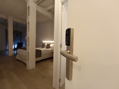 Entrada de apartamento moderno en El Rincón de Sevilla con cerradura digital, puerta abierta mostrando dormitorio con ropa de cama blanca