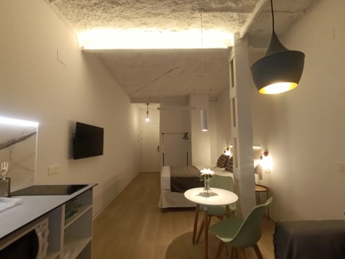 Moderno estudio en Sevilla con salón abierto, cocina, cama, mesa redonda, lámpara colgante y televisor de pantalla plana.