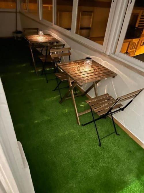 Terraço de hostel ao ar livre do Grupo Lisboa com mesas de madeira, cadeiras, relva artificial verde e corrimões brancos em Lisboa