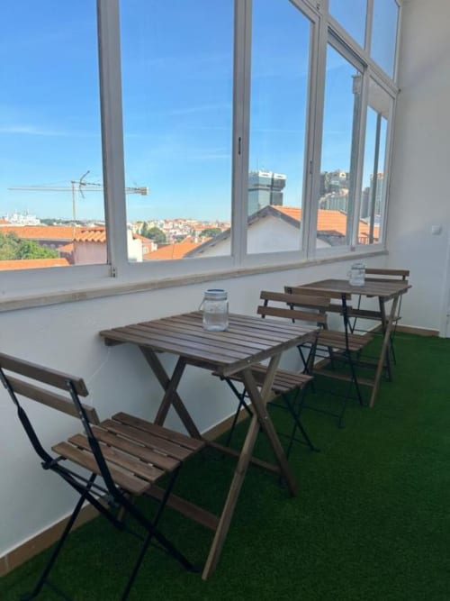 Terraço de hostel em Lisboa com mesas de piquenique, grama verde e vista do skyline da cidade através de grandes janelas