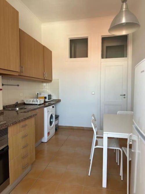 Cozinha e área de refeições modernas do hostel Grupo Lisboa Alojamentos em Lisboa com armários de madeira e cadeiras brancas