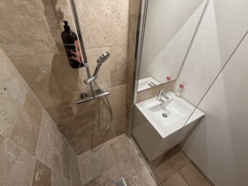 Modern bathroom at Horizon Doré hotel in Gourbeyre with walk-in shower, dual sinks, and neutral tile decor
