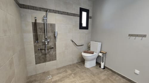 Barrierefreies Badezimmer in den Villas Lantana in Lecci mit begehbarer Dusche, weißem WC und Haltegriffen
