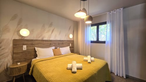 Modernes Schlafzimmer in den Villas Lantana in Lecci mit gelbem Bettzubehör, Pendelleuchten, Holzkopfteil und Stadtblick