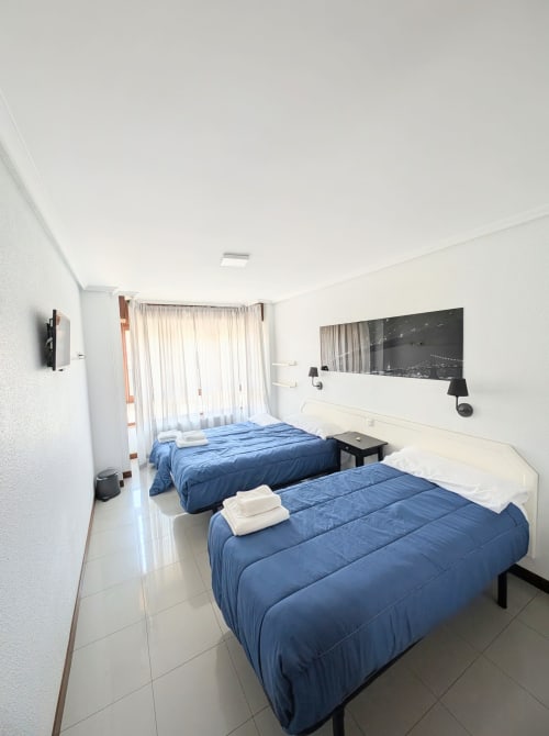Habitación triple con dos camas azules en Alojamiento La Ballena en Santoña, España, con paredes blancas, baño compartido y