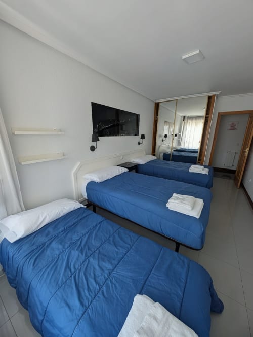 Habitación triple con tres camas azules, almohadas blancas, televisor y espejo en La Ballena B&B de Santoña