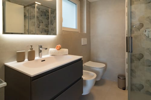 Modern bathroom at Pescara INN with black vanity, white sink, toilet, and glass shower enclosure with sea view window