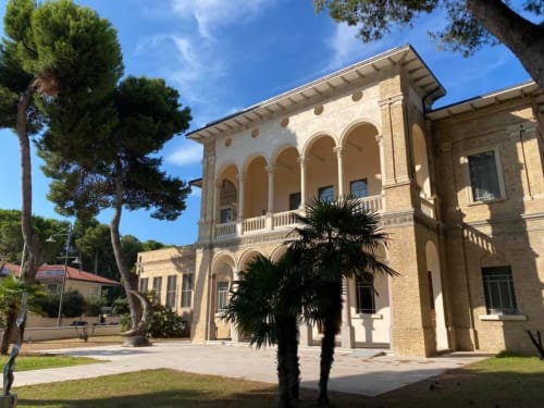 Pescara INN Pineta Retreat: historic brick building with arched columns, palm trees, and garden courtyard in Pescara, Italy