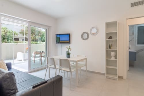 Modern apartment living area at Pescara INN Beach House with dining table, flat-screen TV, garden view through glass doors,