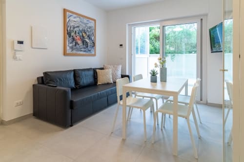 Modern apartment living area at Pescara INN with black sofa, dining table, and garden view through glass doors