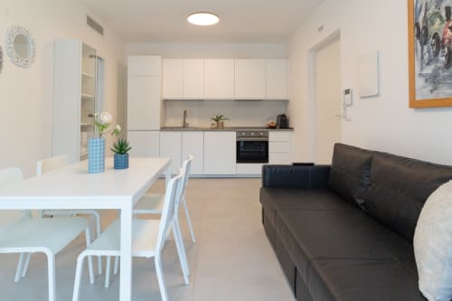 Modern open-plan living area at Pescara INN Beach House with white kitchen, dining table, and dark sofa