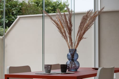 Modern dining area at Pescara INN Beach House with red table, blue vase of dried pampas grass, and garden view through
