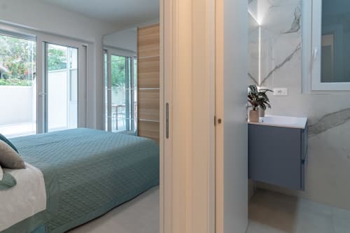 Modern bedroom at Pescara INN Beach House with teal bedding, ensuite bathroom, glass doors to garden, and natural wood