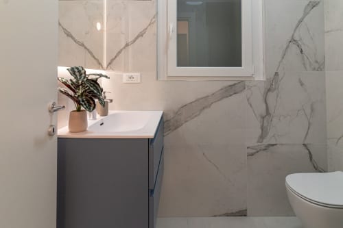 Modern bathroom at Pescara INN Beach House with white sink, dark vanity, marble tile walls, and decorative plant