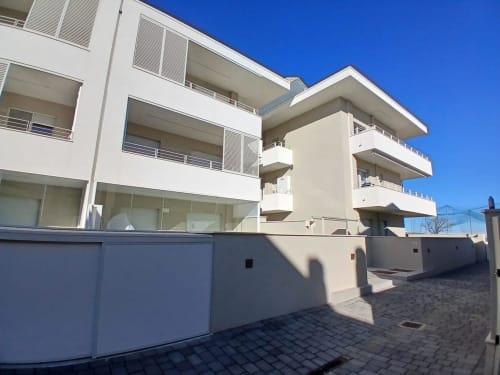 Modern white apartment building at Pescara INN beach house with balconies, parking area, and clear blue sky