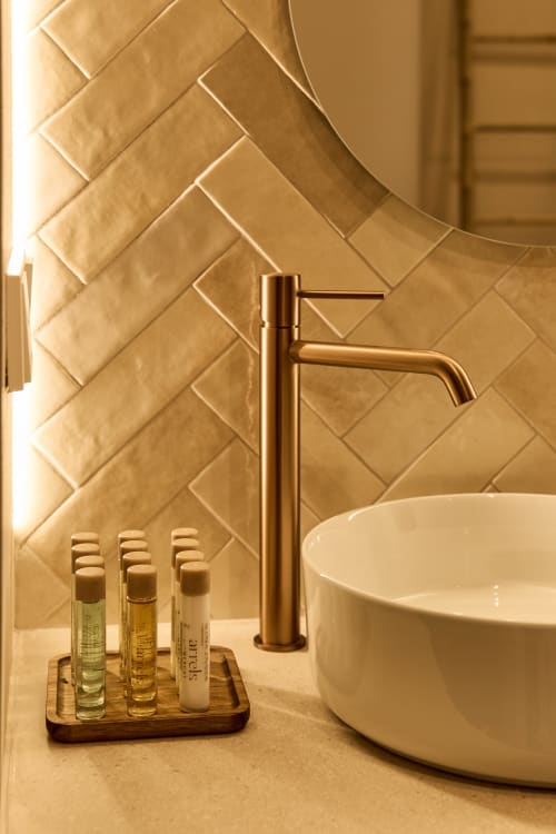 Luxury bathroom vanity at Arrels Mercat Valencia with golden brass faucet, white ceramic sink, herringbone tile backsplash,