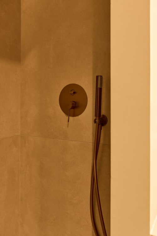 Bronze shower fixtures and valve on beige tile wall in Arrels Mercat apartment bathroom, Valencia