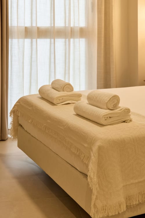 Neatly folded cream towels arranged on a bed at Arrels Mercat apartment in Valencia with sheer curtains and city view window