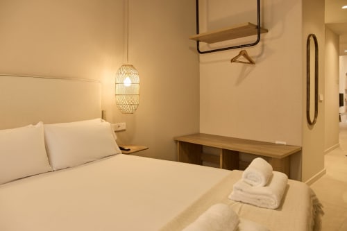 Modern bedroom at Arrels Mercat Valencia apartment with white bedding, wooden desk, pendant lighting, and minimalist décor