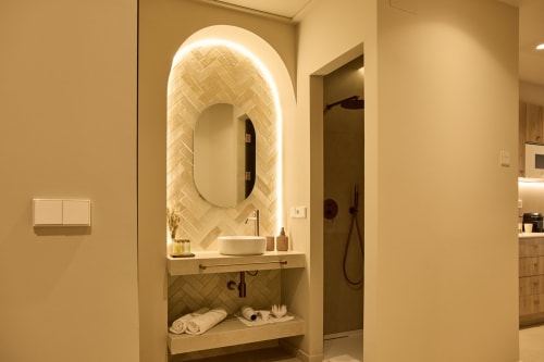Modern bathroom vanity with illuminated oval mirror, white vessel sink, and herringbone tile backdrop at Arrels Mercat