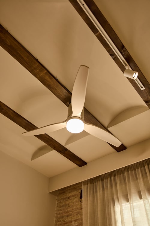 Modern ceiling fan with LED light mounted between exposed wooden beams in Valencia apartment