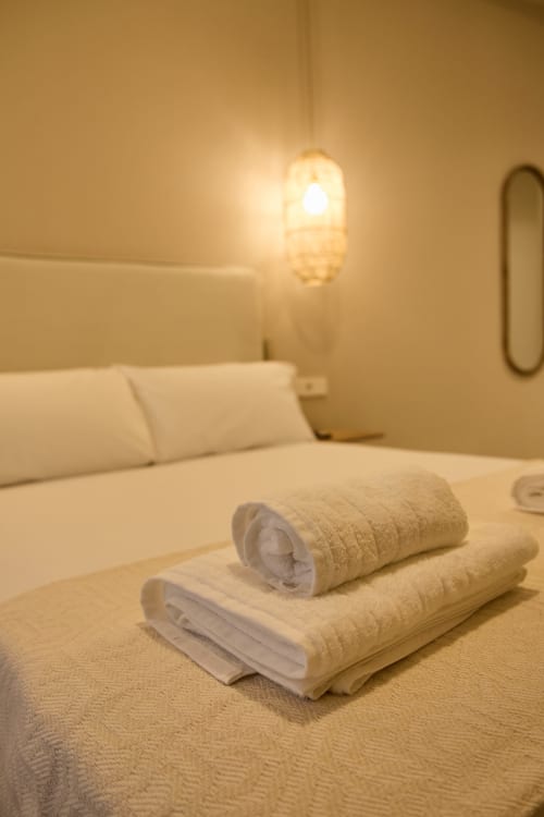 Hotel room at Arrels Mercat Valencia with rolled white towels on bed, modern lighting, and city view apartment setup