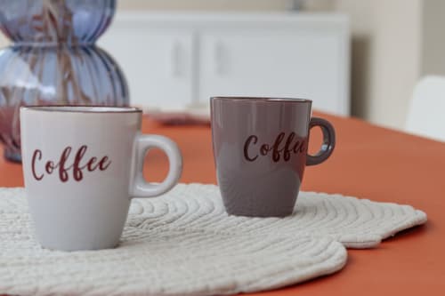 Two coffee mugs on a cream mat at Pescara INN Beach House, set against an orange table with garden view decor