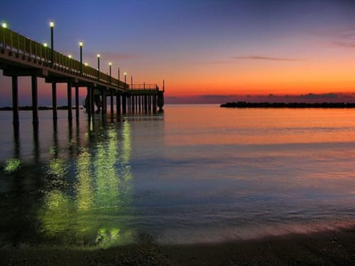 Illuminated pier at sunset over Pescara beach with vibrant orange sky and calm water reflections