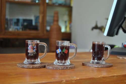 Três canecas de cerveja decorativas com designs tradicionais em porta-copos de madeira na pousada Casa Estrelícia-Dourada Garcês em São